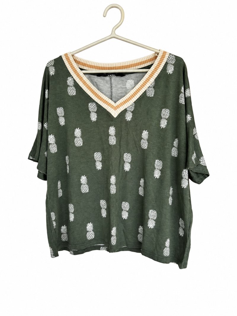 Frente da blusinha verde, com abacaxis estampados e decote em V
